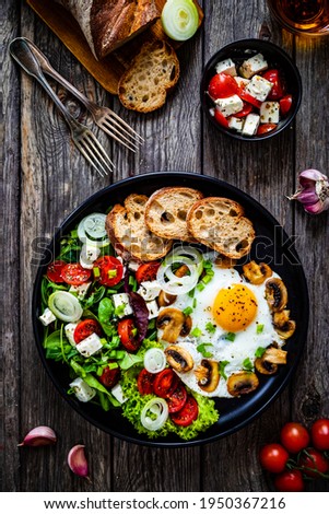 Continental breakfast - sunny side up eggs on white mushrooms, onion and greek salad on wooden table 