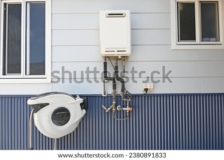 Continuous flow gas hot water heater on the side of a house with hose real