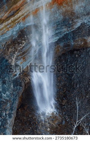 Continuous waterfall flow framed by layered stone cliff.