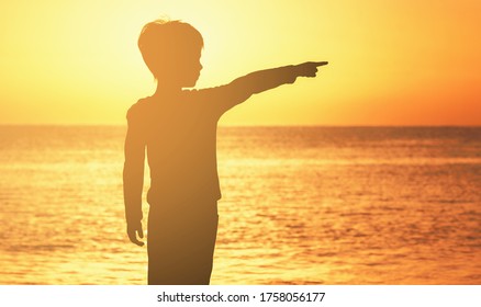 contour of a boy at sunrise sunset on the seashore of the ocean orange sky sea ocean boy shows his finger to the side - Shutterstock ID 1758056177