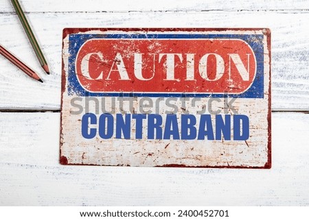 Contraband. Metal CAOTION plate with text on a white wooden background.