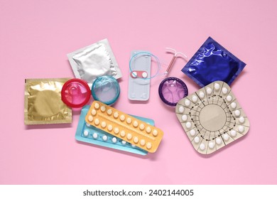 Contraceptive pills, condoms and intrauterine device on pink background, flat lay. Different birth control methods