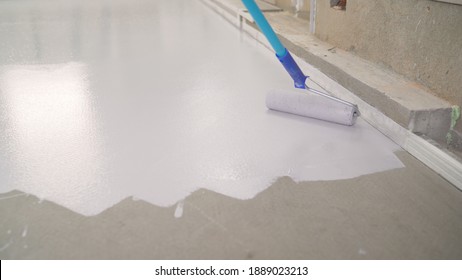 Contract painter painting garage floor to speed up selling of home. Rolling Epoxy Paint on Concrete Floor. House under construction. Worker puts primer on concrete floor.