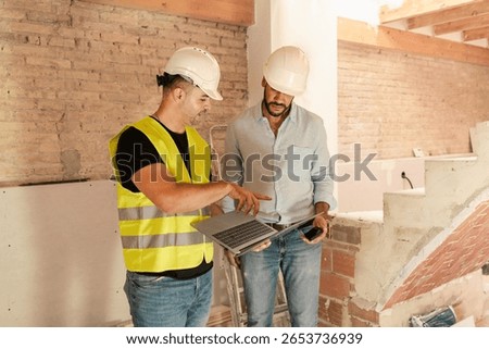 Contractor and engineer using laptop discussing project details during building construction