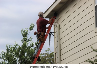 Contractor installing a gutter system on a two story residential house