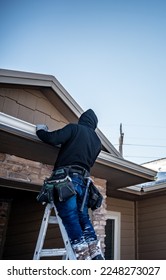 Contractor installing gutters on a residential building in the winter with snow on the roof. - Shutterstock ID 2248273027