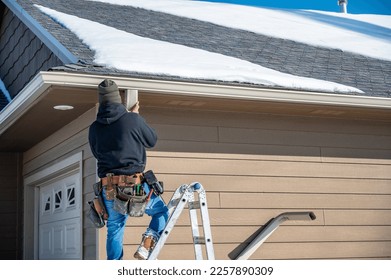 Contractor installing gutters on a residential building in the winter with snow on the roof. - Shutterstock ID 2257890309