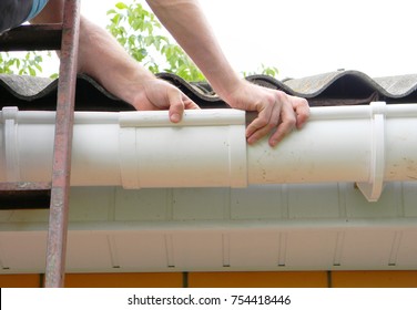 Contractor Installing Plastic Roof Gutter Pipeline. Roofer Install Rain Gutter. 