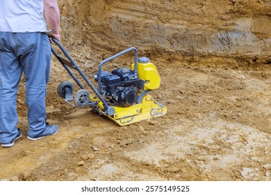 Contractor operates plate compactor on construction site, compacting soil for solid foundation.