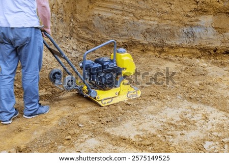 Contractor operates plate compactor on construction site, compacting soil for solid foundation.