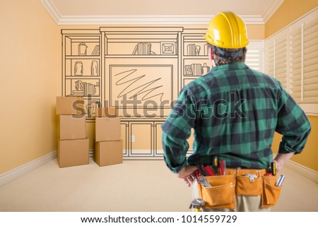 Contractor Standing Indoors with Moving Boxes Looking At Line Drwaing of Entertainment Unit on Wall.