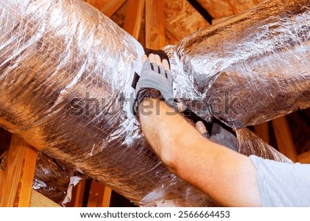 Contractor worker adjusts insulation around ductwork in residential attic, ensuring proper sealing efficiency.