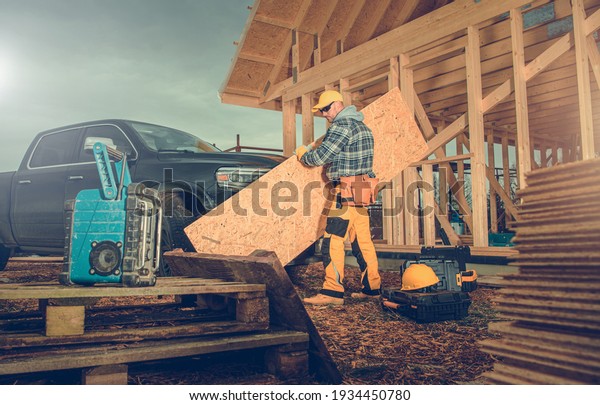 Contractor Worker\
Moving Piece of Plywood in Newly Built Wooden House Construction\
Site. Industrial Theme.\
