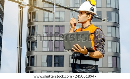 Contractor, Young man engineer checking information from laptop and commands with talking on radio call with colleague, Foreman working on building site and monitor antenna, urban development in city