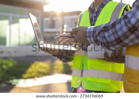 Contractors discussing building plans using laptop and blueprint.