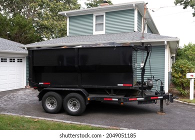 A contractors dumpster is on a trailer for easy hauling in their customers driveway.