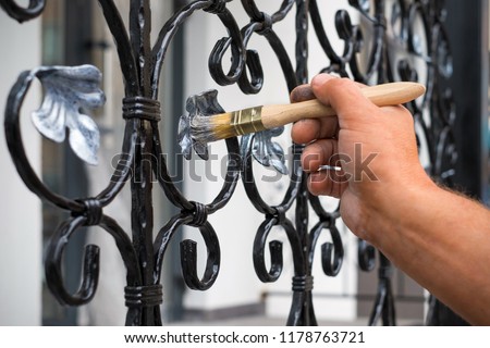 Contractor's hand with brush that painting metal fence. 