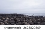 The contrast between solid coastal rocks, soft waves, and a muted gray sky highlights the rugged beauty of the untouched shoreline.  