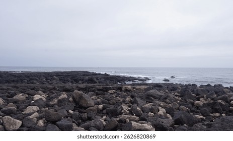 The contrast between solid coastal rocks, soft waves, and a muted gray sky highlights the rugged beauty of the untouched shoreline.  