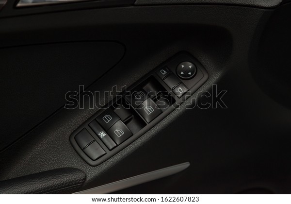 The control\
buttons for opening and closing windows of doors and electric\
controls and settings of mirrors on the door in black with leather\
upholstery in a luxury modern\
car.