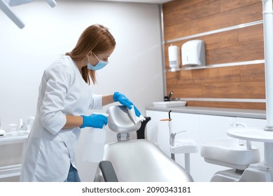 Control Of Epidemic, Infection And Virus Prevention. Nurse Working In Stomatology Clinic, Disinfect Dental Chair With Sanitizer After Each Patient, Wipes Work Surfaces In Cabinet