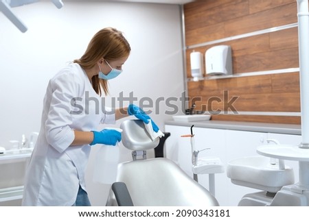 Control of epidemic, infection and virus prevention. Nurse working in stomatology clinic, disinfect dental chair with sanitizer after each patient, wipes work surfaces in cabinet