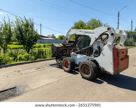 A re -control loader drops asphalt on the side of the road.