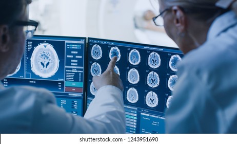 In Control Room Doctor and Radiologist Discuss Diagnosis while Watching Procedure and Monitors Showing Brain Scans Results, In the Background Patient Undergoes MRI or CT Scan Procedure. - Shutterstock ID 1243951690