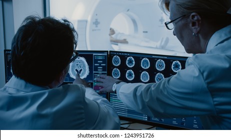 In Control Room Doctor and Radiologist Discuss Diagnosis while Watching Procedure and Monitors Showing Brain Scans Results, In the Background Patient Undergoes MRI or CT Scan Procedure. - Powered by Shutterstock