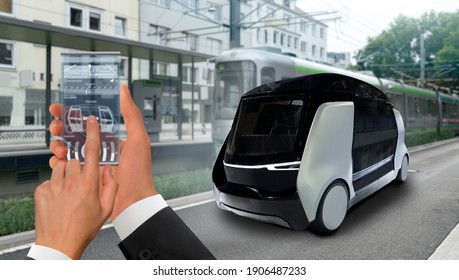 Control Of Self Driving Taxi By Mobile App. Hand With Phone On A Background Of Autonomous Shuttle.