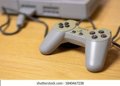 A Controller For The Original Playstation, Plugged Into The Console, On A Wood Floor.