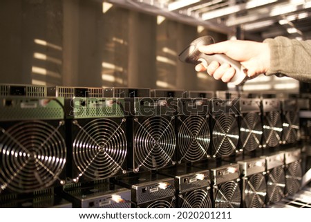 Controller in uniform scans ASIC bitcoin miners with barcode scanner in warehouse. Warehouseman working in storage room. Worker scans barcodes of power supply units in service repair center.