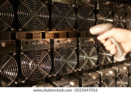 Controller in uniform scans ASIC bitcoin miners with barcode scanner in warehouse. Warehouseman working in storage room. Worker scans barcodes of power supply units in service repair center.