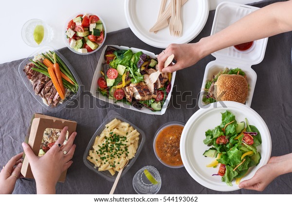 Convenient takeaway takeout food\
for party, overhead spread of assorted food with hands serving\
up