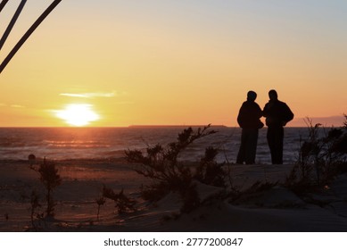 A conversation between two dark silhouettes of people against the backdrop of a sunset on a Baltic Sea beach.