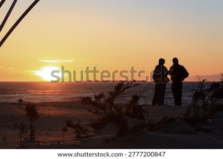 A conversation between two dark silhouettes of people against the backdrop of a sunset on a Baltic Sea beach.
