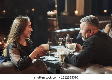 Conversation Between Young And Older Generation. Family Friends Have Nice Evening Near The Fireplace In Luxury Modern Restaurant.