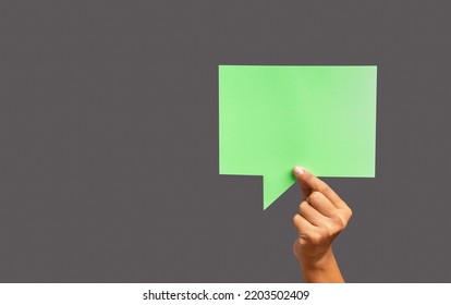Conversation bubble concept. Close-up of hand holding a green speech bubble against a gray background in the studio. Close-up photo. Space for text - Shutterstock ID 2203502409