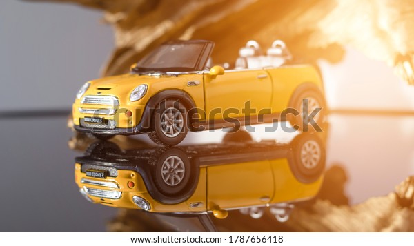 Convertible model yellow Mini\
Cooper on a gray background. A yellow toy car rides on a light\
background, reflected on a mirrored floor. July 31, 2020, Belarus\
Gomel.