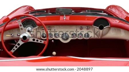 The convertible top is down in the horizontal view of the white dashboard of vintage red sportscar.  All the gauges and the steering wheel are in beautifully maintained or restored condition.