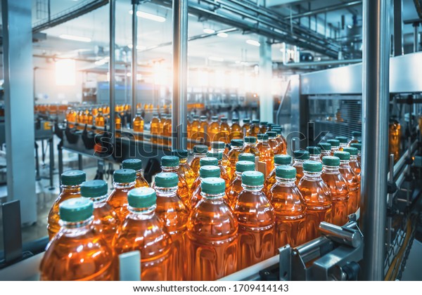 Conveyor belt, juice in\
bottles, beverage factory interior in blue color, industrial\
production line.