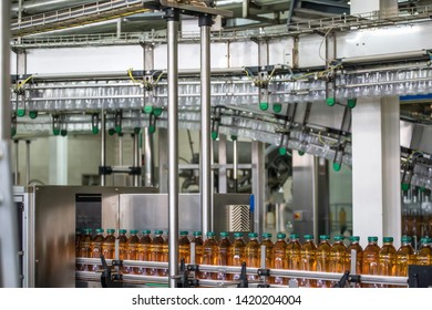 Conveyor belt or line in beverage plant with modern industrial machine equipment. Plastic bottles with fresh organic juice in factory interior.