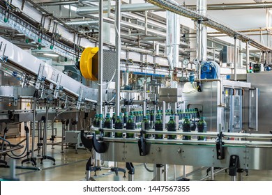 Conveyor belt or line in beverage plant with modern automated industrial machine equipment. Plastic PET bottles in factory interior.