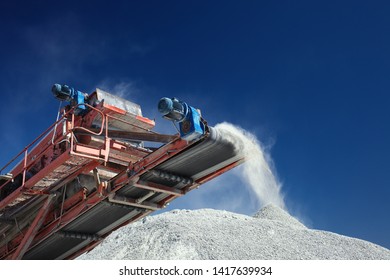 Conveyor Belt Of A Working Mobile Crusher Machine, Close-up, With Blown Away By The Wind White Stone Dust Against A Blue Sky.