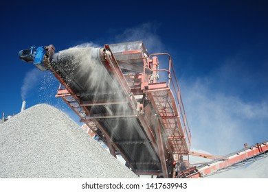 Conveyor belt of a working mobile crusher machine, close-up, with blown away by the wind white stone dust against a blue sky.