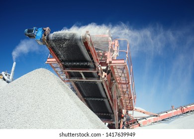 Conveyor Belt Of A Working Mobile Crusher, Close-up, With Blown Away By The Wind White Stone Dust Against A Blue Sky.