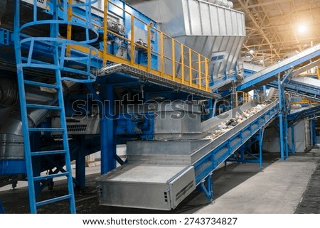 Conveyor belts at a waste sorting facility are moving mixed materials for efficient recycling. Workers oversee the operation to ensure proper sorting and processing of waste materials.