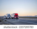Convoy of a industrial grade commercial professional transportation of different big rig semi trucks with semi trailers driving on the straight highway road at twilight time in California