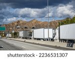 Convoy of industrial grade commercial transportation of different big rig semi trucks with semi trailers standing on the at the weighing station with scales for weighing along the axes in California