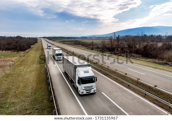 Convoy of\
Three White transportation  trucks in line as a caravan or convoy\
on a country highway under a blue\
sky